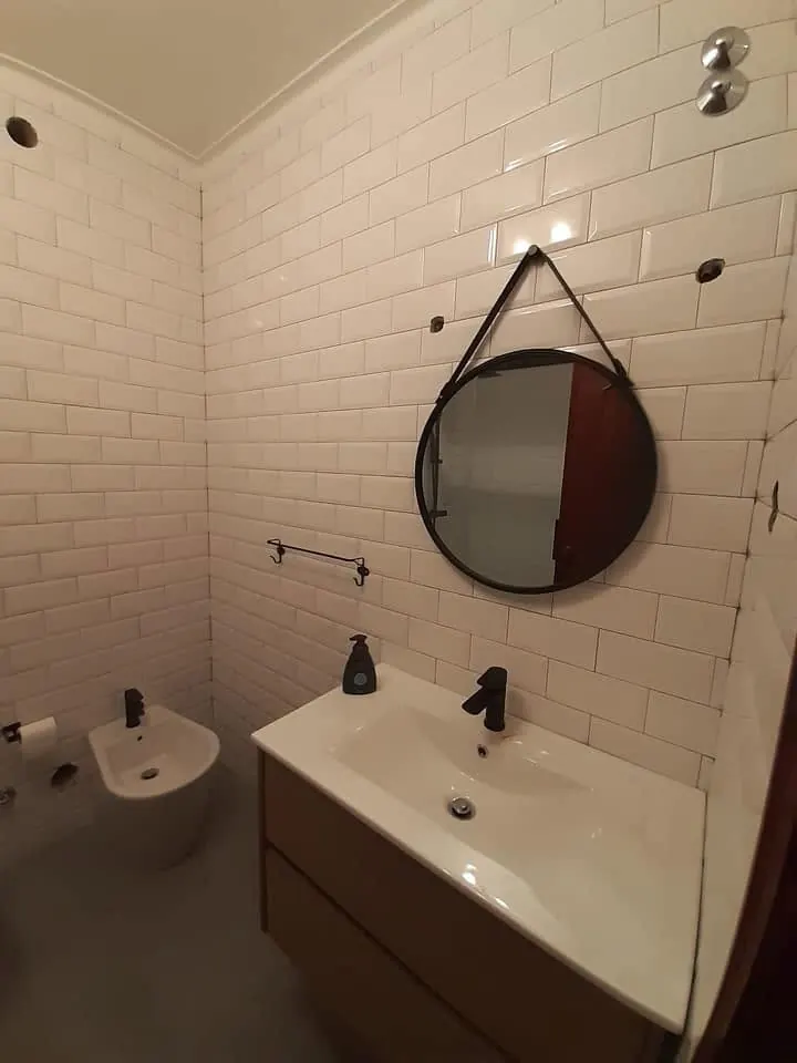 Casa de banho remodelada com azulejo metro branco e espelho redondo