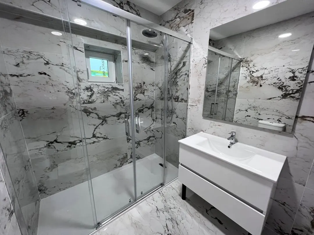 Casa de banho remodelada com duche em vidro e revestimento efeito mármore