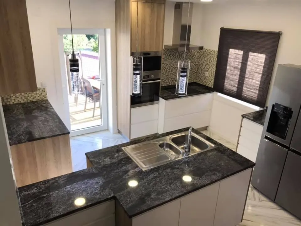 Cozinha remodelada com bancada em granito escuro e móveis brancos